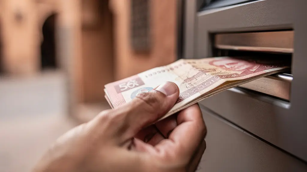 Gros plan sur la main d'une personne retirant des billets à un distributeur dans une rue marocaine