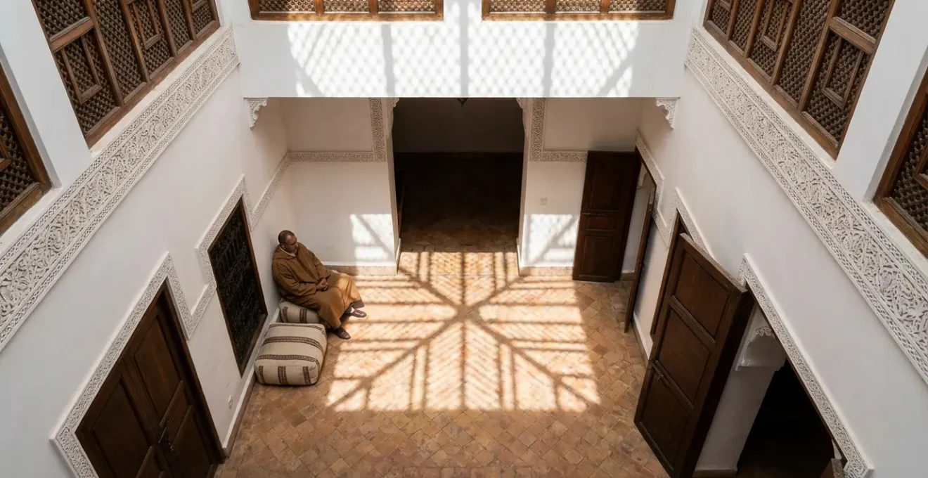 Patio intérieur d'un dar traditionnel marocain baigné dans une lumière tamisée avec jeu d'ombres géométriques